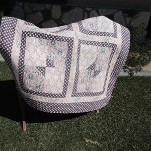 May include: A pink and black quilt with a floral pattern and polka dots. The quilt is folded and displayed on a wooden stand.