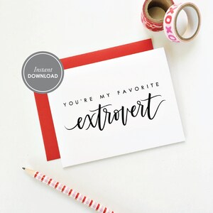 Op de afbeelding: Een witte kaart met zwarte tekst die "You're my favorite extrovert" zegt. De kaart ligt op een wit oppervlak met een rode envelop en een potlood met roze en witte strepen.