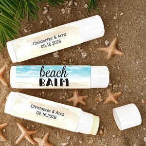 May include: Three white lip balm tubes with custom labels on a sandy surface, surrounded by starfish. One label reads "beach BALM" with a beach scene. Two other labels read "Christopher & Anna 09.16.2026".