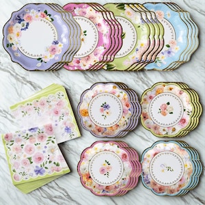 May include: A collection of floral-themed party supplies, including scalloped-edge paper plates in pastel colors like lavender, pink, green, and blue, with gold trim. Matching napkins are also included, featuring a similar floral design.