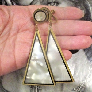 May include: A pair of gold tone clip-on earrings with white mother of pearl triangle shaped drops. The triangles have a black outline.