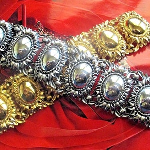 May include: Two gold and silver tone bracelets with oval-shaped stones set in a floral design. The bracelets are on a red background.