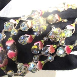 May include: A multi-strand necklace with clear crystal beads and pink and green flower-shaped beads.