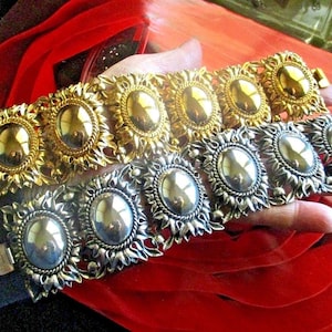 May include: Two gold and silver tone bracelets with oval-shaped stones. The bracelets are made of metal and have a floral design.