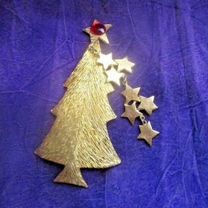 May include: A gold-tone Christmas tree brooch with a red jewel at the top and a dangling chain of gold stars.