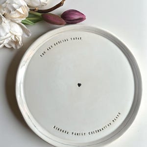 May include: White ceramic plate with the text "YOU ARE SPECIAL TODAY" and "LINDNER FAMILY CELEBRATION PLATE" in black lettering. A small black heart is centered on the plate. The plate is surrounded by a thin gray line.
