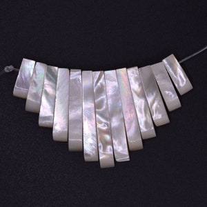May include: A strand of white iridescent mother-of-pearl shell beads, each bead is rectangular and has a slightly curved edge. The beads are strung on a clear thread.