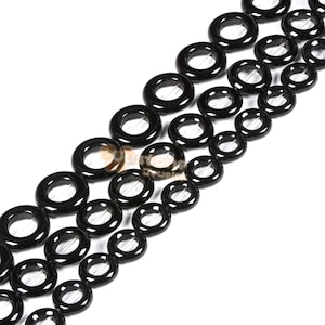 May include: A strand of black onyx beads, each bead is a ring with a hole in the centre. The beads are arranged in a staggered pattern.