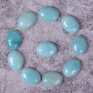 May include: Ten oval-shaped, light blue gemstones arranged in a circle on a gray textured surface.