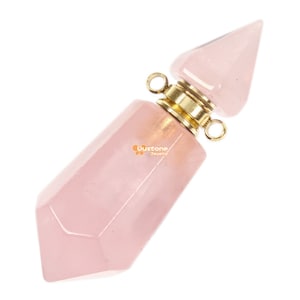 Puede incluir: Un tapón de botella de cristal de cuarzo rosa con una tapa y un lazo de metal dorado. El tapón de botella tiene forma de cristal puntiagudo.