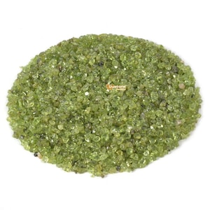 Puede incluir: Una vista cercana de un montón de pequeñas piedras preciosas de peridoto verde claro. Las piedras tienen una forma irregular y una apariencia ligeramente translúcida.