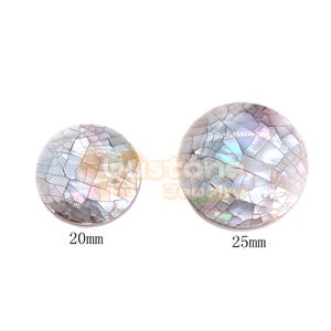 May include: Two circular shell cabochons featuring a mosaic pattern of iridescent, pearlescent fragments in shades of white, gray, and soft pink. The left piece is labeled 20mm and the right piece is labeled 25mm, indicating their respective diameters.