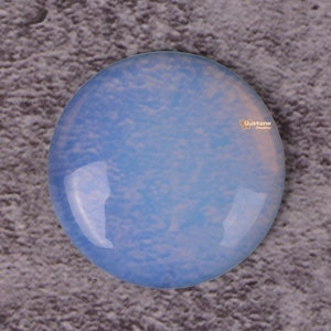 May include: A round, light blue opal cabochon with a cloudy, white pattern. The opal is smooth and polished.