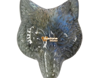 Puede incluir: Un colgante de cabeza de lobo tallado en piedra de labradorita. La piedra tiene un brillo iridiscente azul y gris.
