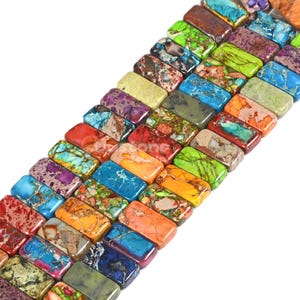 May include: A strand of colorful, rectangular, polished gemstone beads. The beads are arranged in a row, with the colors varying from green, blue, red, orange, and purple.
