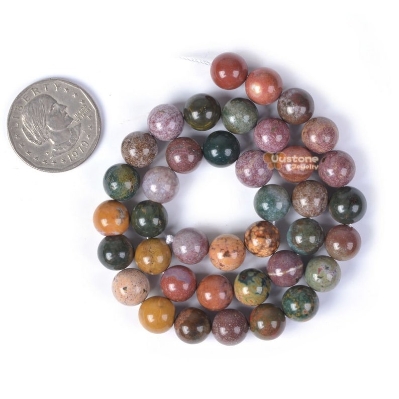 Pu&ograve; includere: Una collana di perline rotonde in pietra naturale multicolore. Le perline sono circa delle dimensioni di una moneta da 10 centesimi di euro. Le perline sono un mix di marrone, verde, rosso e viola.