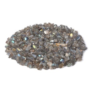 May include: A pile of iridescent grey labradorite gemstone chips. The chips are various sizes and shapes, with a shimmering, rainbow-like effect.