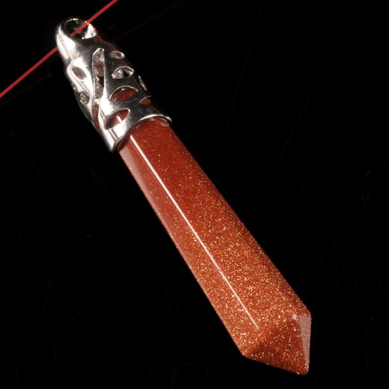 May include: A silver pendant with an intricate design, featuring a red-brown gemstone with a pointed tip.