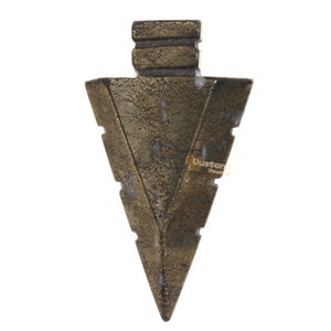 May include: A gold-coloured metal arrowhead pendant with a textured surface. The arrowhead is pointed at the bottom and has a flat top with three ridges.