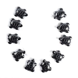 May include: A strand of black turtle beads, each with a detailed shell design. The beads are strung on a clear thread and arranged in a circle.