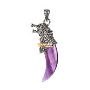 Könnte beinhalten: Ein silberfarbener Anhänger mit einem Wolfskopf-Design, der auf einem großen, lila, klauenförmigen Stein sitzt. Der Wolfskopf weist aufwendige Details auf, und der Stein hat einen leuchtenden Lilaton. Der Anhänger hängt an einer silbernen Schlaufe.