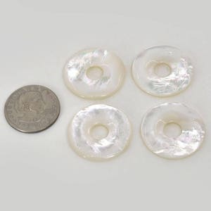 Puede incluir: Cuatro anillos de n&aacute;car blanco iridiscente con un agujero en el centro. Los anillos son aproximadamente del tama&ntilde;o de una moneda de 25 centavos de d&oacute;lar estadounidense.