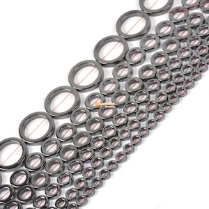 May include: A collection of black hematite donut beads of varying sizes, strung on a thin copper wire. The beads are arranged in a graduated pattern, with the largest beads at the top and the smallest beads at the bottom.