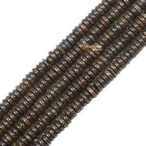 Puede incluir: Una hebra de cuentas de madera fosilizada marrón. Las cuentas son redondas y tienen un acabado liso y pulido. Están enhebradas en un cordón elástico transparente.