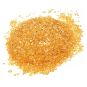 May include: A collection of small, irregularly shaped, translucent amber-coloured glass pieces. The pieces are scattered across a white surface. The text "Uustone Jewelry" is visible in the image.