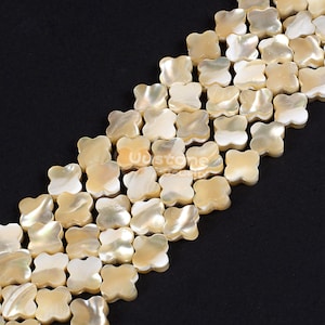 Puede incluir: Una hebra de cuentas de concha blancas y crema en forma de trébol de cuatro hojas. Las cuentas están enhebradas para crear un collar o una pulsera.