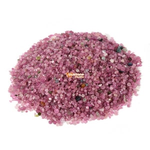 Könnte beinhalten: Ein Haufen rosa, roter und grüner Turmalin-Edelsteine. Die Edelsteine sind klein und rund und auf einem weißen Hintergrund verstreut.