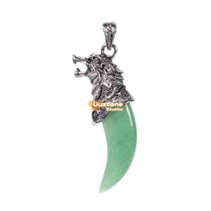 Könnte beinhalten: Ein silberner Wolfskopf-Anhänger mit einem grünen Jade-Fangzahn. Der Anhänger ist ein detailliertes Design mit einem Wolfskopf mit offenem Maul und scharfen Zähnen. Der Jadestein ist hellgrün und hat die Form eines Fangzahns.