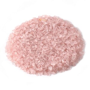 May include: A close-up of a pile of pink rose quartz chips. The chips are small and irregular in shape, and they have a translucent appearance.