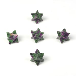Op de afbeelding: Vijf groene en paarse stervormige kristallen, ook wel bekend als Merkaba-kristallen, zijn symmetrisch gerangschikt op een witte achtergrond.