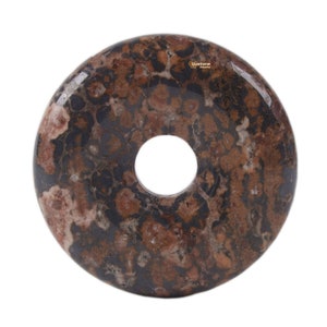 Puede incluir: Una piedra de color marrón y negro con forma de donut con un agujero en el centro. La piedra tiene un patrón moteado con manchas marrones, negras y blancas.