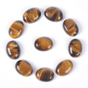Puede incluir: Diez piedras de ojo de tigre ovaladas en varios tonos de marrón y dorado. Las piedras están dispuestas en círculo sobre un fondo blanco.