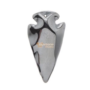 May include: A polished, metallic grey arrowhead pendant with a hole at the top for a necklace. The pendant has a smooth, reflective surface and the text "Oustone Jewelry" is visible on the front.