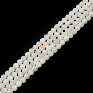 Op de afbeelding: Close-up van meerdere strengen witte, ronde kralen tegen een zwarte achtergrond. De kralen zijn gelijkmatig van grootte en lijken gemaakt van een glad, gepolijst materiaal. De kralen zijn in parallelle lijnen geregen. De afbeelding is goed belicht.