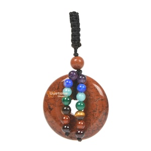 Op de afbeelding: Een hanger van rode jaspis met een zwart koord en zeven chakra- kralen. De kralen zijn van amethist, lapis lazuli, turquoise, groene aventurijn, tijgeroog, carneol en rode jaspis.