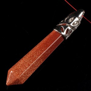May include: A red-brown, pointed, crystal pendant with a silver filigree setting. The pendant is made of sunstone and has a sparkly, glittery texture.