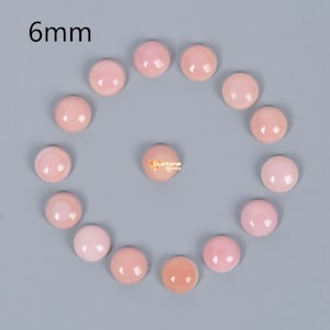 May include: A collection of 14 pink shell cabochons, each measuring 6mm in diameter. The cabochons are arranged in a circle on a grey background.