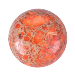 May include: A close-up of a round, orange and brown jasper stone with a marbled pattern. The stone is smooth and polished.