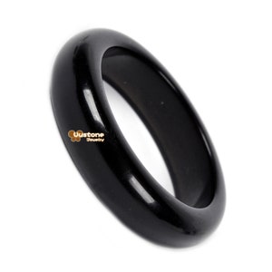 May include: A black, polished, round bangle bracelet. The bangle is smooth and shiny.