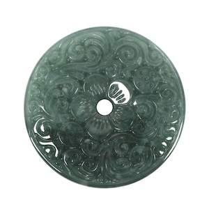 Puede incluir: Un colgante redondo de jade con un diseño floral tallado en color verde claro.