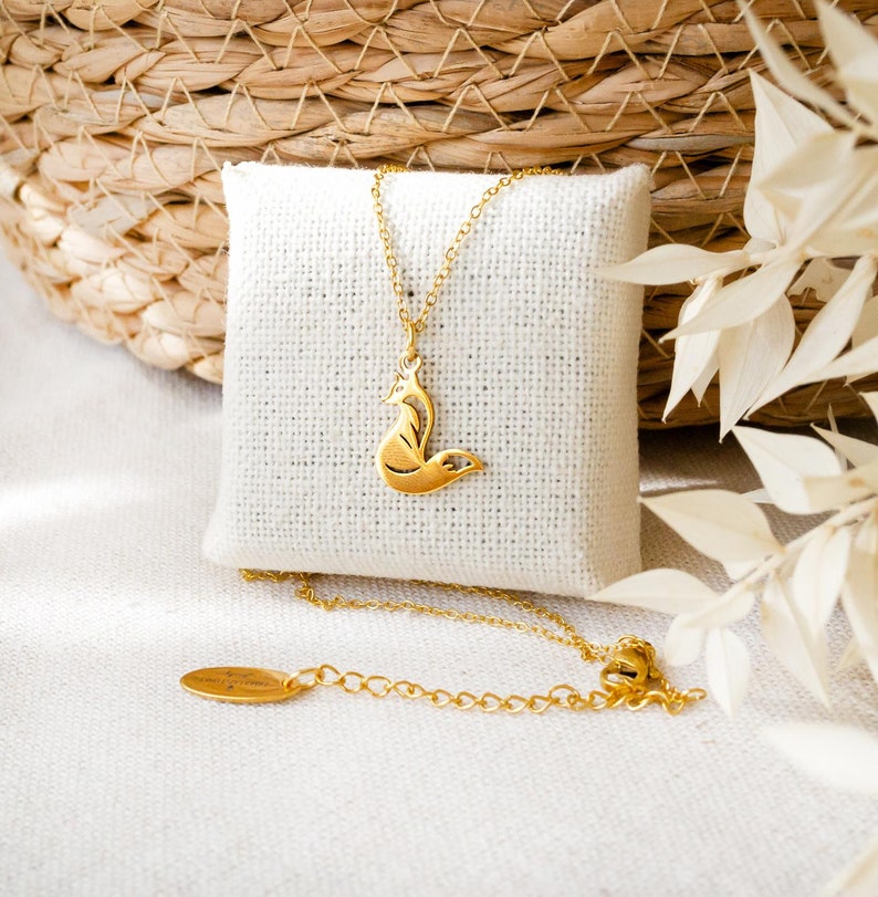 K&ouml;nnte beinhalten: Eine goldfarbene Halskette mit einem zierlichen fuchs-f&ouml;rmigen Anh&auml;nger an einer feinen Kette. Die Kette verf&uuml;gt &uuml;ber ein verstellbares Element mit einem kleinen ovalen Metallanh&auml;nger am Ende, das ein poliertes Finish und eine Tier-Silhouette zeigt.