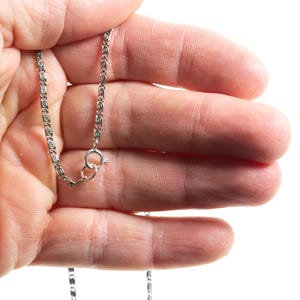Puede incluir: Un collar de cadena de metal plateado que presenta un patr&oacute;n repetitivo de eslabones intrincados en forma de volutas u ondas. La cadena est&aacute; asegurada con un mecanismo de cierre de resorte circular, mostrando un acabado met&aacute;lico pulido.