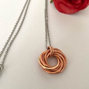 May include: A silver chain necklace with a copper pendant. The pendant is a circle made of multiple intertwined copper wires.