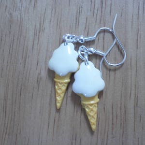 May include: A pair of silver ice cream cone earrings with white ice cream and yellow cone details.