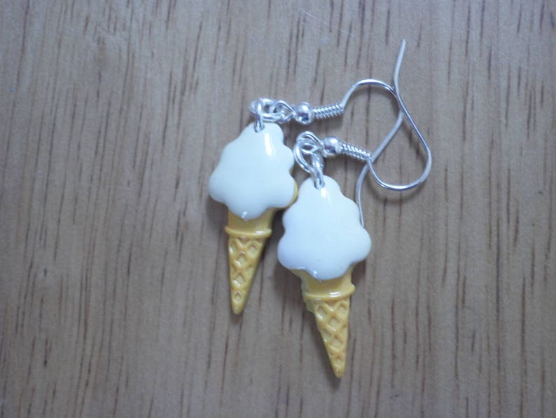 May include: A pair of silver ice cream cone earrings with white ice cream and yellow cone details.