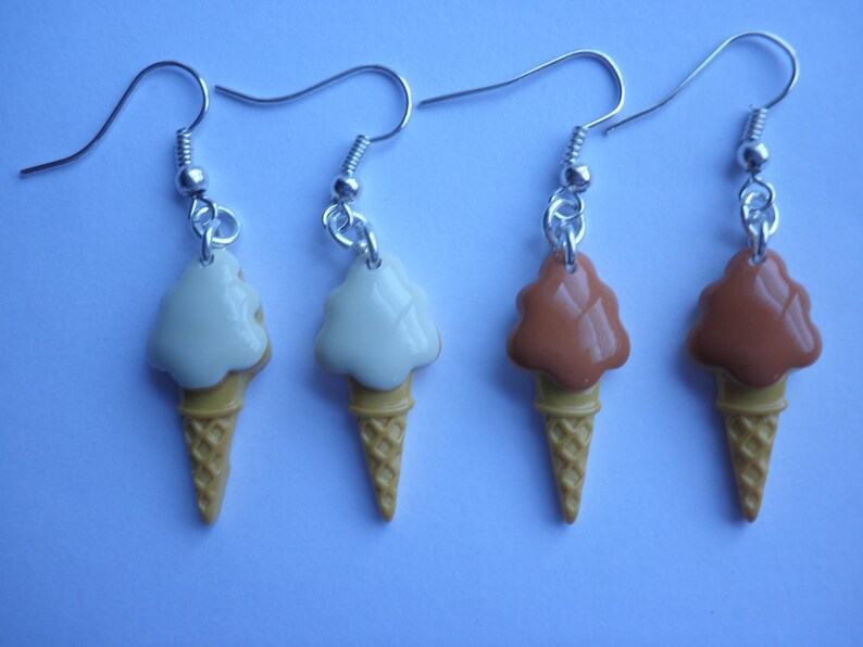 May include: Four pairs of ice cream cone earrings. Two pairs are white ice cream with a brown cone and two pairs are brown ice cream with a brown cone.